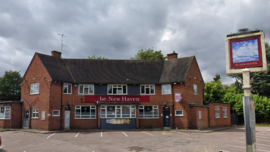 The New Haven pub with its board sign to the right-hand side. The sign has partially fallen off and the door have been boarded shut. 