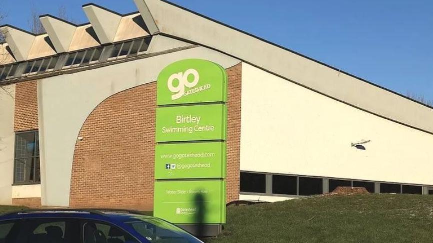 Outside of the swimming centre which has a green sign saying 'Go Gateshead'