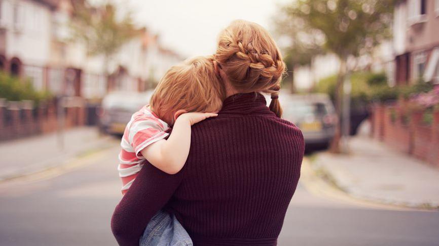 Rear view of a woman carrying a child in a street. Their faces are hidden.