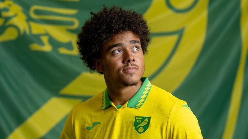 Norwich City striker Jovon Makama, pictured with a club flag.