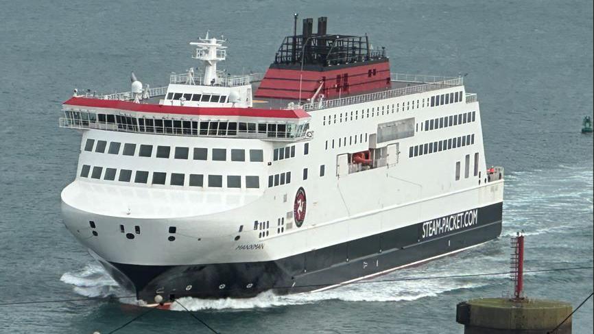 The Manxman ferry arriving in Douglas Harbour. Its livery is white, red and black and it has STEAMPACKET.COM written on its side.