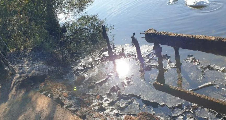 The burned platform partially in the water. The wood is blackened and the sun is reflected in the water