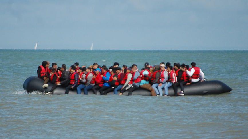 A large inflatable boat is packed with people wearing red life jackets.