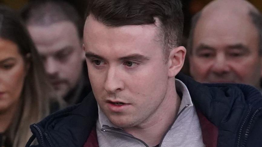 Ryan Casey. He has short dark hair, wearing a navy coat and grey half zip.
