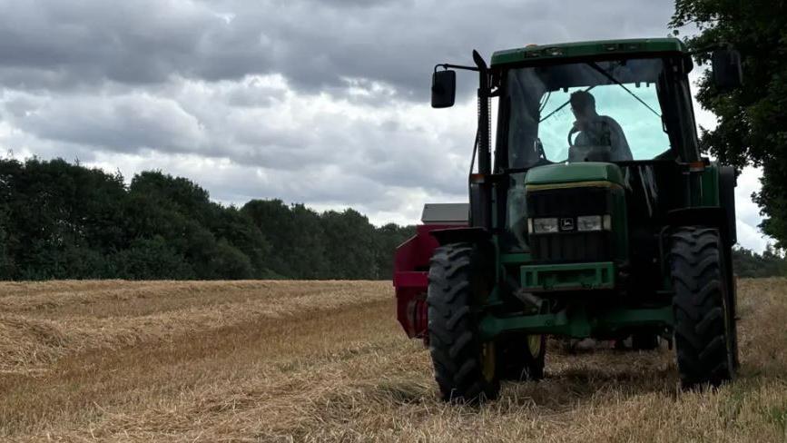 A picture of a green tractor in a wheat field. 