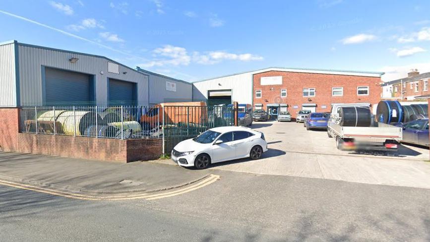 Vehicles parked in yard, surrounded by industrial estate units