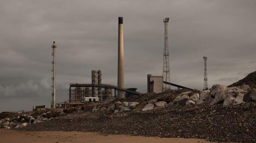 Conveyor belts and chimneys on the site are captured from nearby Aberafan beach