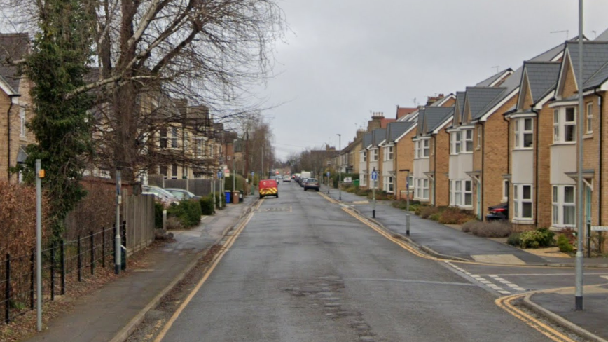 A street view of Aldermans Drive - a residential street with terrace houses on either side of the road