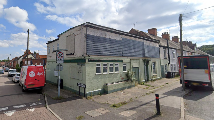 An old brick building painted green and white with metal sheets across the windows