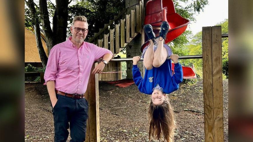 Headteacher Glyn Jones of Blue Coat Primary School wearing a pink shirt next to Flora, a year 5 student, in school uniform and upside down.