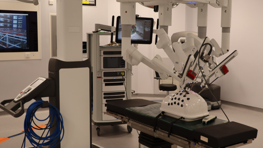 The white robotic equipment has a long surgical device inserted into a plastic shell on an operating table. 