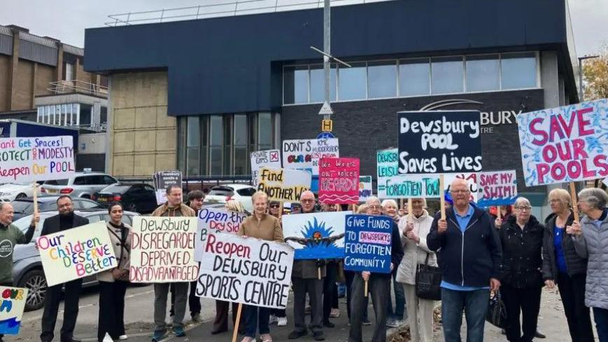 Protest outside a swimming pool threatened with closure in November - around 20 members of the public holding placards with slogans like: 'Our children deserve better' and 'Dewsbury disregarded, deprived, disadvantaged'.