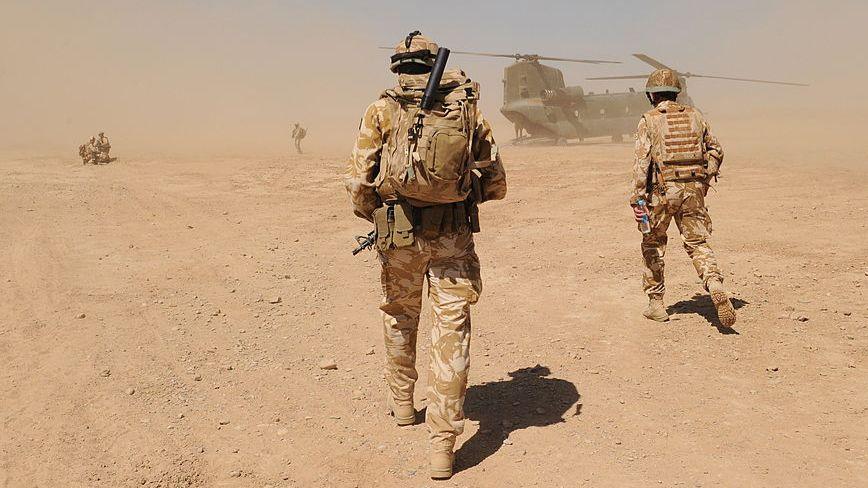 British soldiers in uniform walk across a dusty, desert landscape towards a military helicopter near the Pimon military camp in Nad-e Ali district of Helmand province in March 2010.