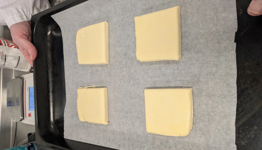 Hands holding a tray with raw rolled out pastry on it but into 4 smaller squares.
