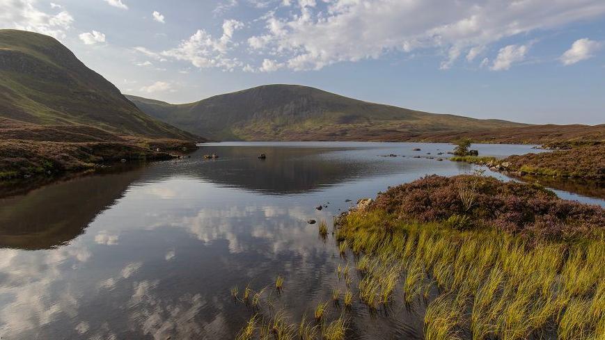landscape scene featuring the waters of a large loch surrounded by hills and moorlands under the a bright daylight sky