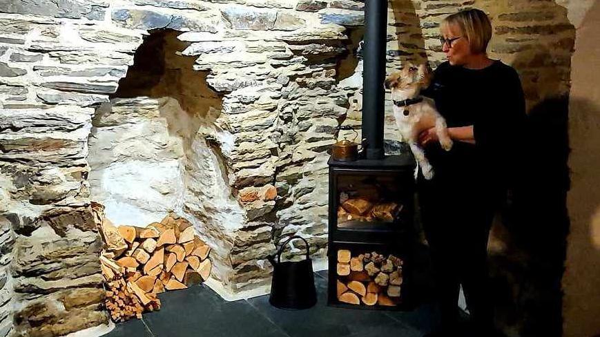 Amanda holding her dog Eric next to the log burner in their cottage