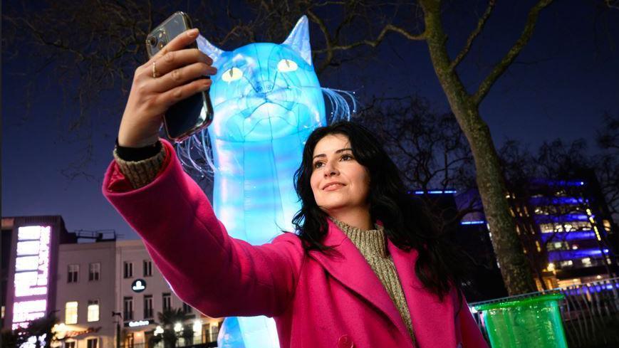 A female member of the public takes a selfie in front of a large, inflatable blow-up blue cat