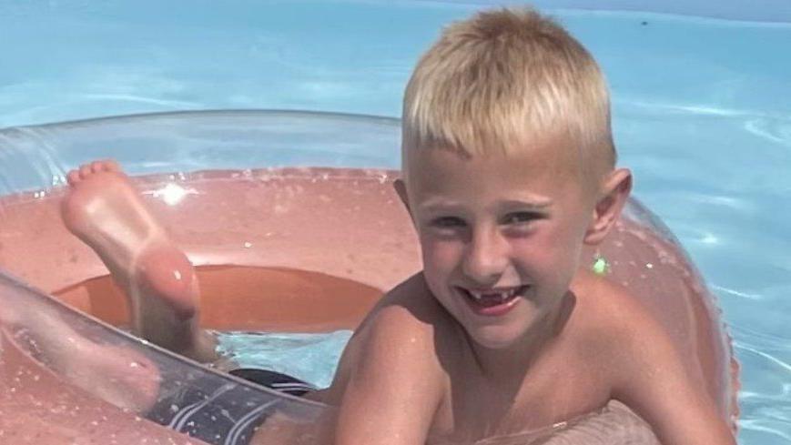 Freddie Farrow, who is blond, smiling and floating on an inflatable doughnut in a swimming pool.