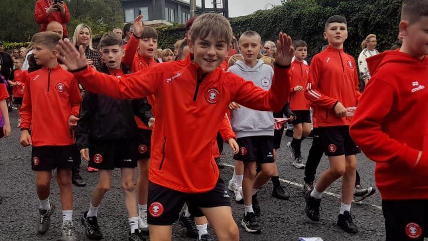 A group of young footballers wearing eam colours walk through the streets of Derry