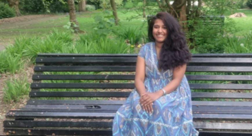 A woman with brown hair and wearing a blue dress sat on a park bench.