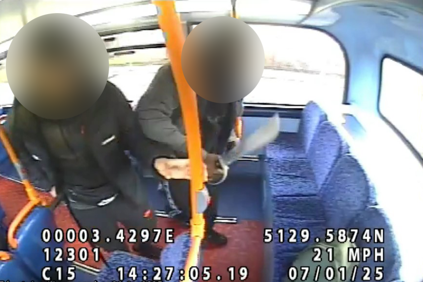 CCTV still taken from inside the bus showing two youths with blurred faces holding a machete. A rucksack can be seen on the back seat