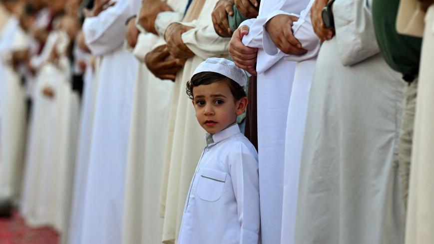 A little boy looks surrounded by worshippers looking out at the camera