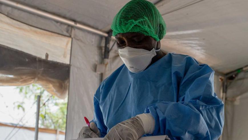 An image of a doctor wearing a white face mask and a blue medical apron.