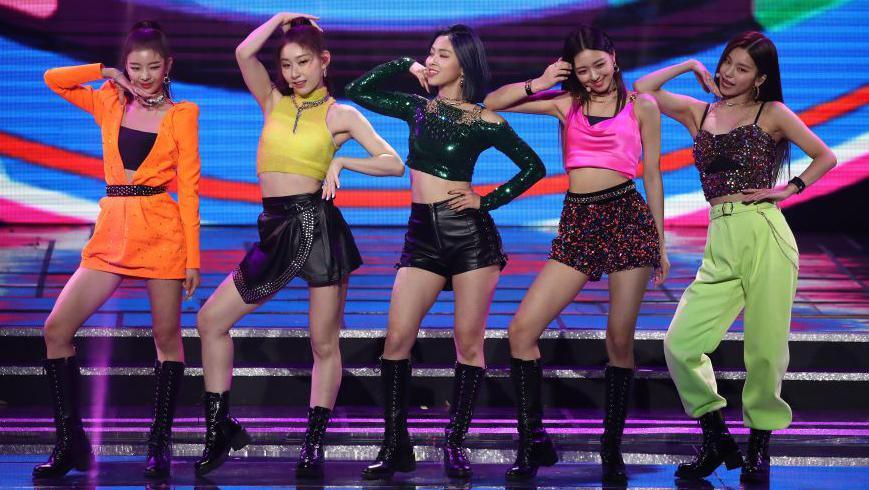 Pop group Itzy pose on stage, wearing brightly-coloured neon outfits