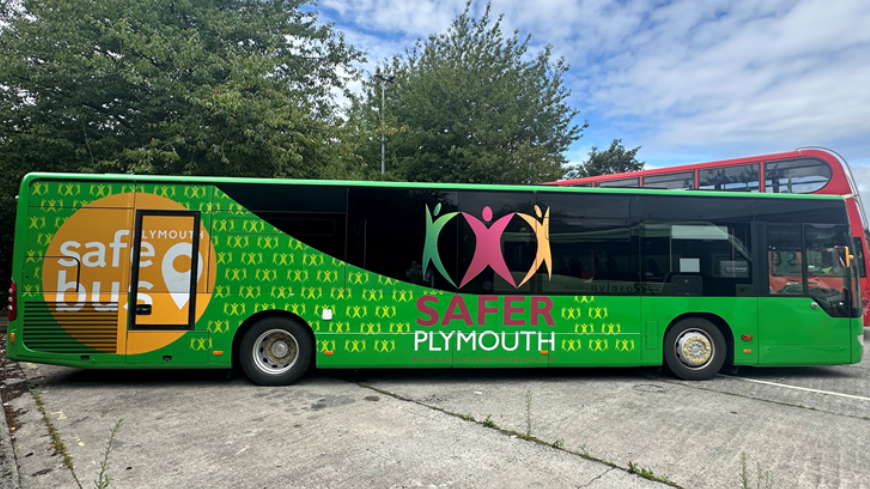 A view of the side of the bus. The bus is green and has stickers promoting Safer Plymouth
