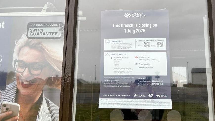 Soidhne air doras Bhanca na h-Alba am Baile a' Mhanaich ag innse do luchd-cleachdaidh gum bi e a' dùnadh