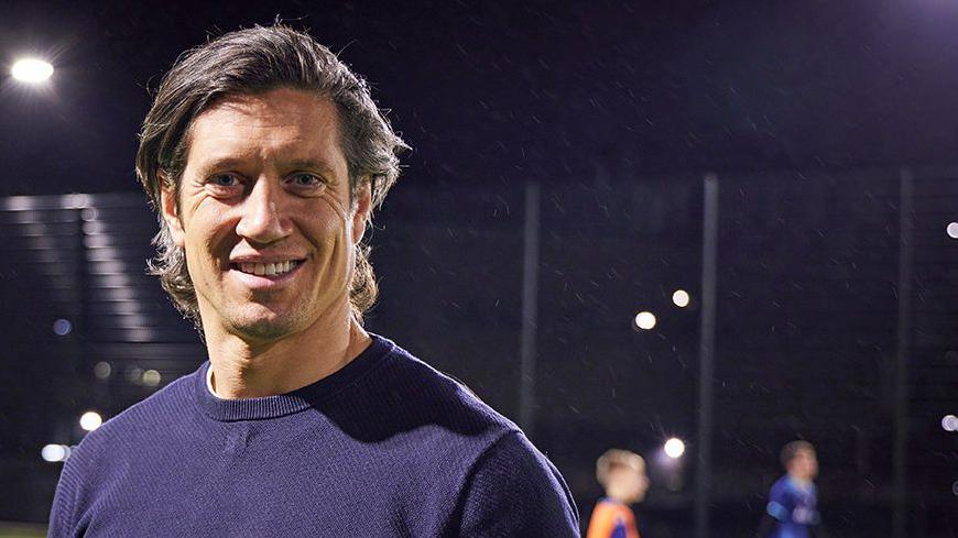 BBC broadcaster Vernon Kay smiling wearing a navy round neck long sleeve top smiling as he joins in a football session with youngsters at Be The Change organisation which offers young people sport sessions