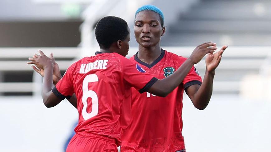 Rose Kadzere spreads her arms wide to embrace Malawi team-mate Temwa Chawinga, who is also spreading her arms to allow the players to clasp hands. Both players are visible from waist up wearing red Malawi kits. Kadzere faces away from camera while Chawinga, who has short dyed blue hair, has a serious expression on her face