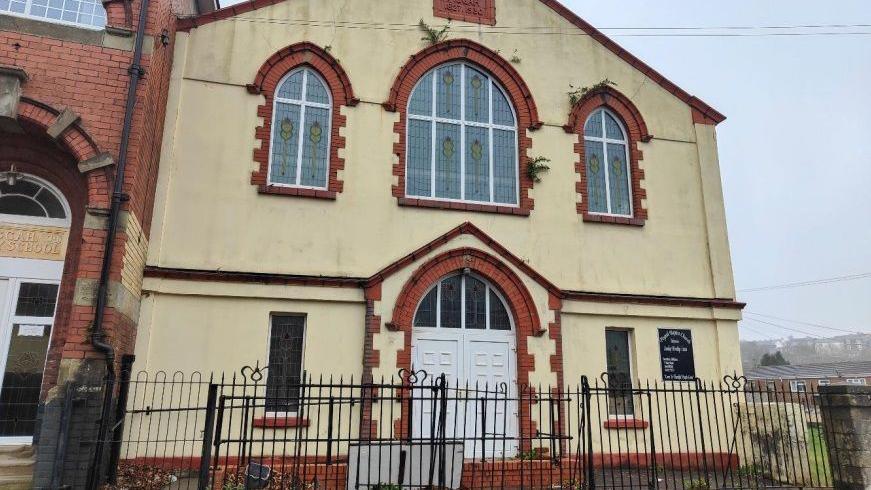 Pisgah Baptist Church in Talywain. It is at the end of a street. The church is painted off-white and has red brickwork around the door and windows