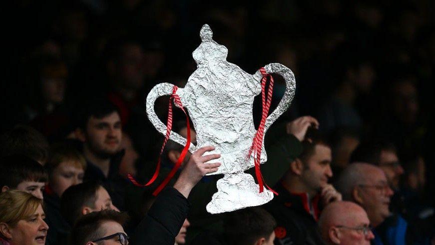 Tinfoil FA Cup trophy held up by a fan