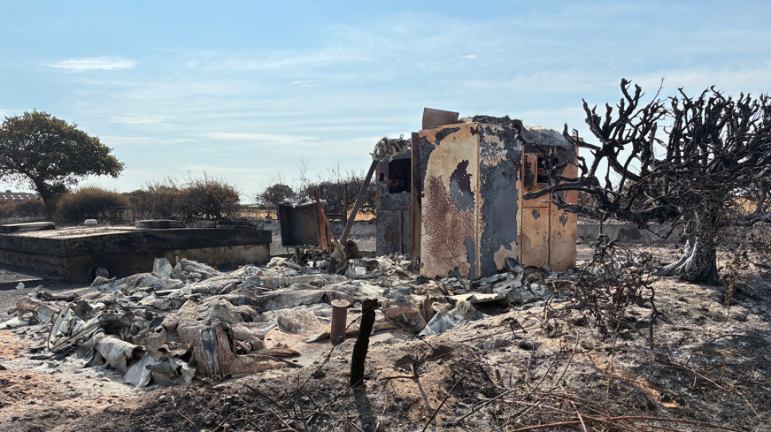 Remains of a small building surrounded by burnt grey remains on charred ground.