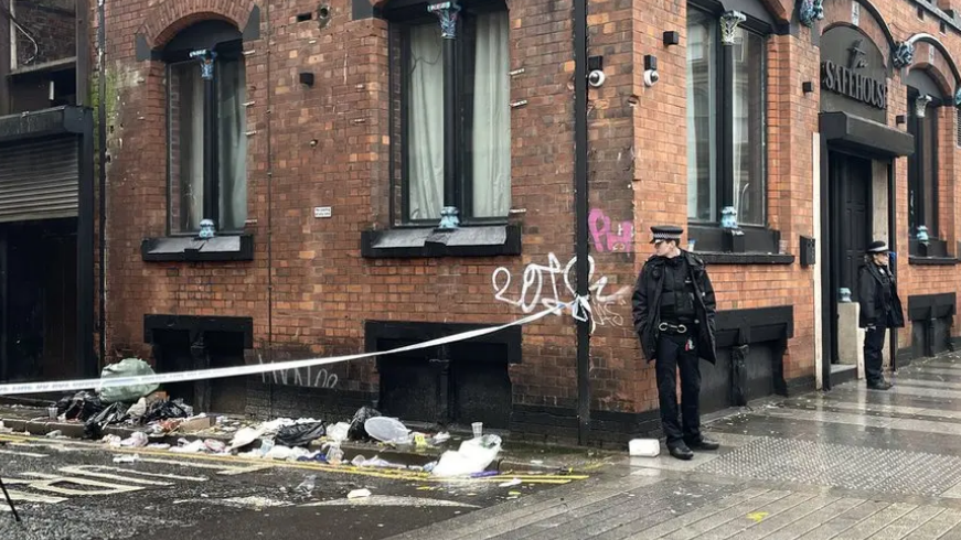 Two police officers stand outside the Safe House nightclub in Liverpool's Whitechapel area. A police cordon blocks off a rubbish-strewn alleyway.