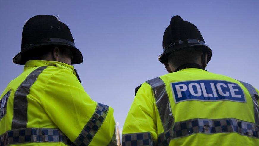 A stock image of two police officers faced away from the camera with blue sky behind
