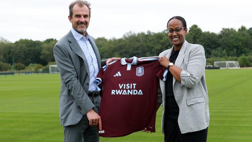 Aston Villa president of business Francesco Calvo and Janet Karemera, CEO of the Rwanda Convention Bureau, hold up an Aston Villa shirt with Visit Rwanda as sponsor
