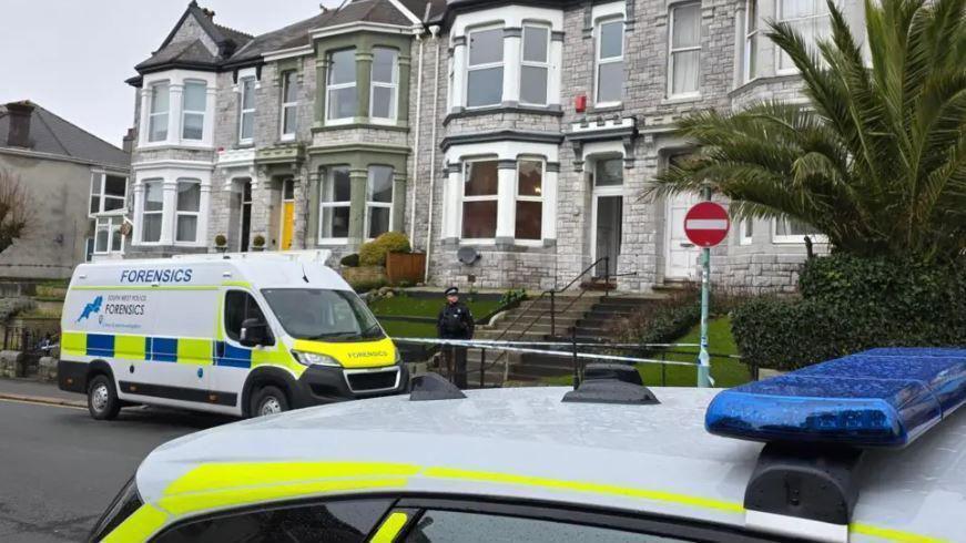 A view of police cars outside a grey stoned house.