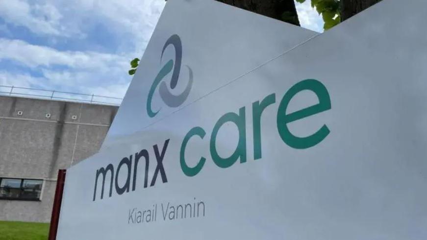 A close up of a large white sign, with blue and green writing, that reads Manx Care.