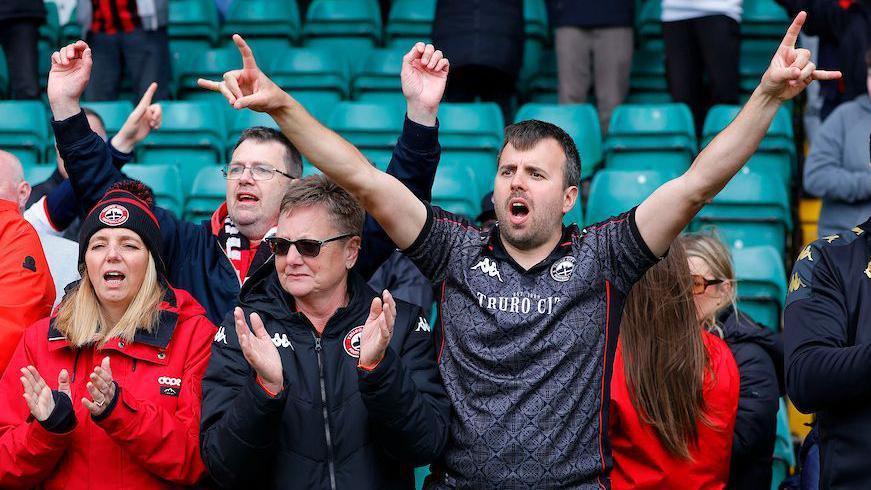 Truro City fans with their arms in the air while singing towards their players after a match.