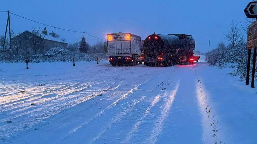 Two lorries attempt to travel down a rural snow-covered road