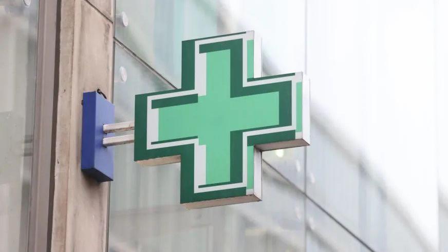 A green cross pharmacy sign attached to a building