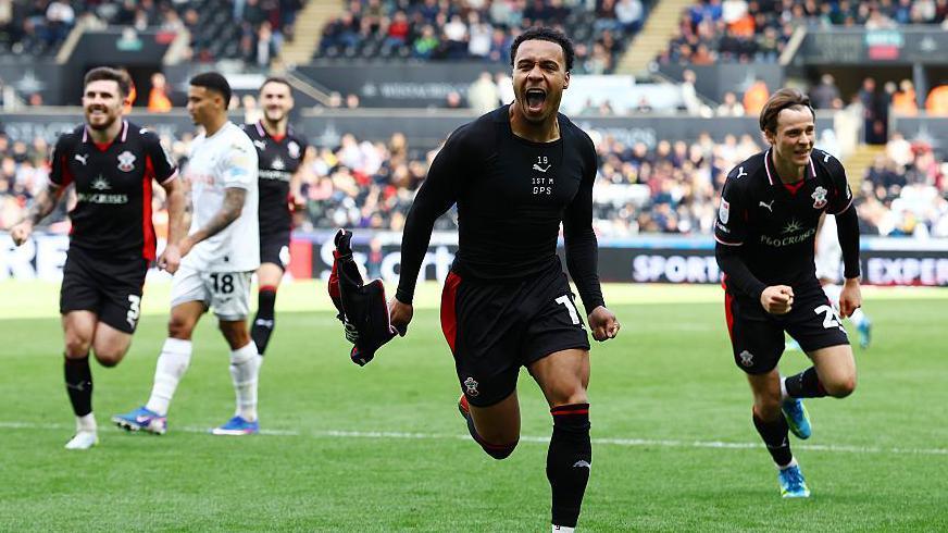 Cameron Archer (centre) runs with his fists clenched and his shirt in his right hand after scoring for Southampton 