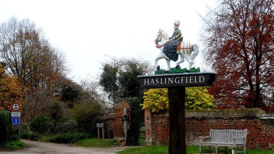 Village sign for Haslingfield with a knight riding on a horse on top of the black-and-white sign.