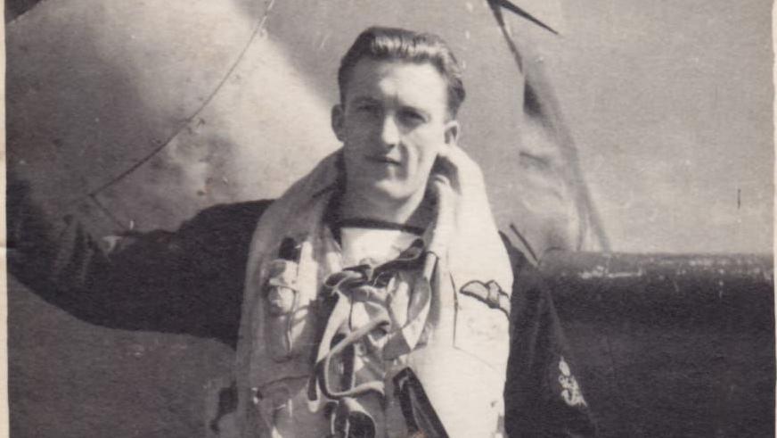 An old black and white photo of Petty Officer Smith in navy uniform standing beside a plane. 