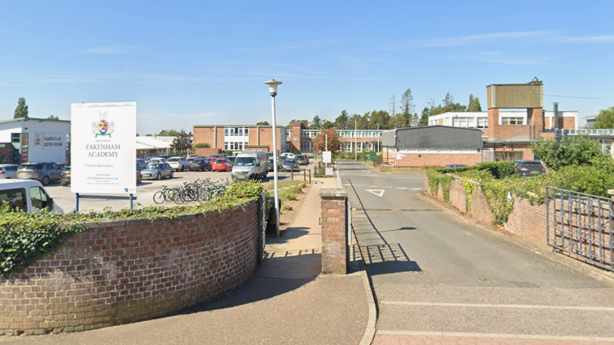 The entrance driveway to Fakenham Academy. The school building is in the background and is two-storey. In the foreground is a car park.