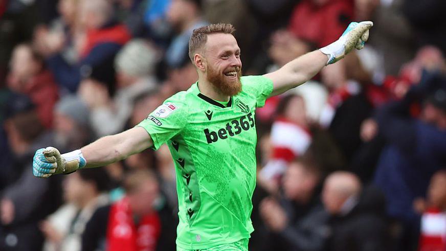 Stoke goalkeeper Viktor Johansson smiles and stretches his arms out in celebration 