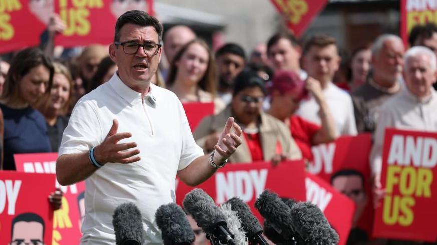 Andy Burnham mewn crys polo gwyn yn annerch torf o gefnogwyr - mae sawl yn yn dal arwyddion gyda'r logo 'Andy for Us'