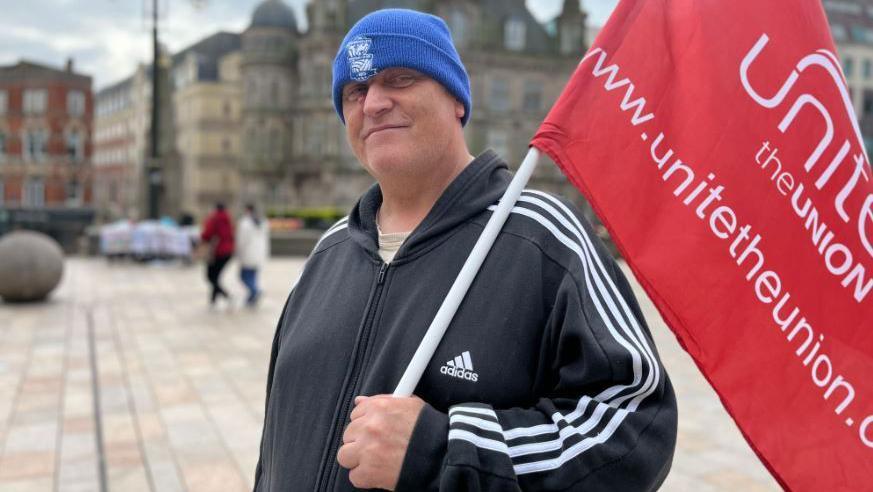 A man wearing a black sports jacket holds a red unite flag.